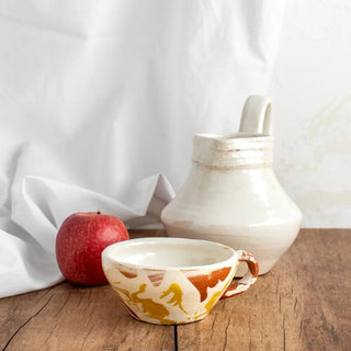 Taza de cerámica amarilla y blanca junto con jarra egipcia y manzana. Real Fábrica