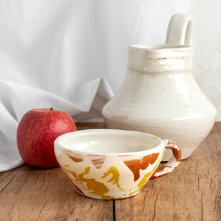 Taza de cerámica amarilla y blanca junto con jarra egipcia y manzana. Real Fábrica