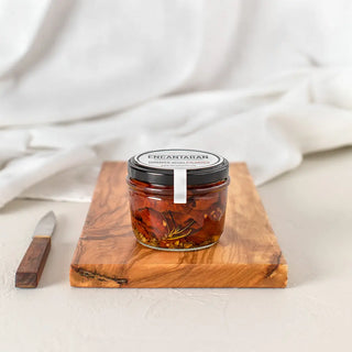 Tarro de cristal de tomates secos procedente de los pirineos sobre una tabla de madera y un cuchillo. Real Fábrica.