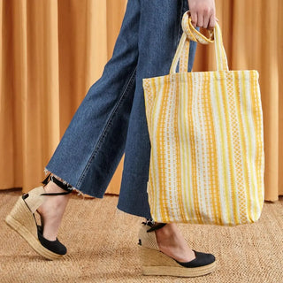 Foto de mujer llevando en su mano una bolsa tote bag alpujarra amarilla. Real Fábrica.