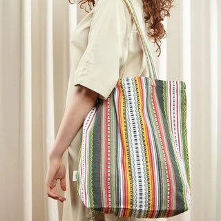 Foto de mujer de perfil llevando en su hombro una bolsa de tela marrón, amarillo, rojo y verde de eturel. Real Fábrica.