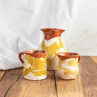 Vaso con asa en color amarillo y blanco junto con una jarra y una taza en los mismos colores. Real Fábrica
