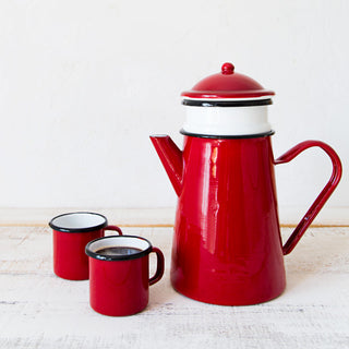 Cafetera de peltre esmaltado roja con filtro junto a dos tazas esmaltadas a juego.