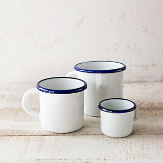 Taza blanca mini de peltre junto a dos tazas esmaltadas blancas de mayor tamaño.