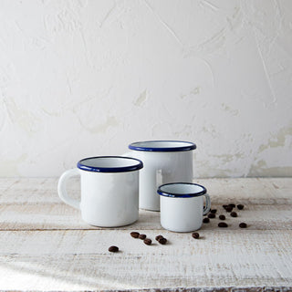 Comparativa de taza blanca mini de peltre con otras tazas esmaltadas de distintos tamaños y granos de café.